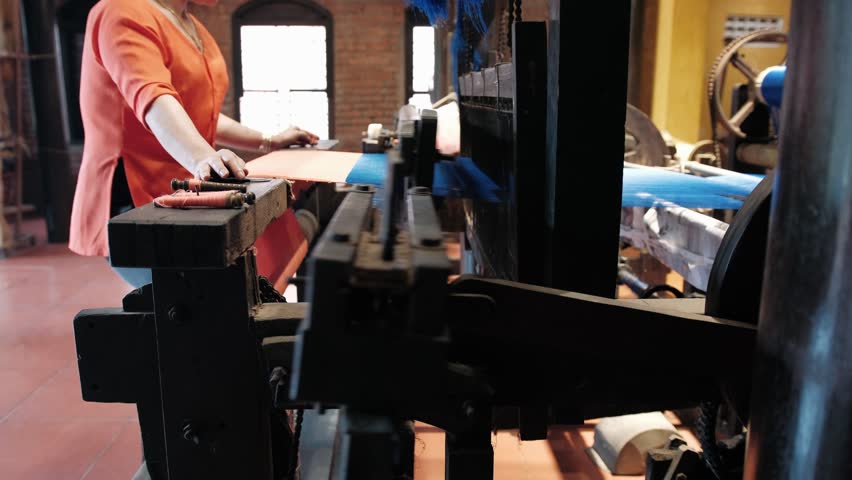 Vietnam woman working on a traditional mechanical loom, weaving colorful blue and orange silk threads in a factory.