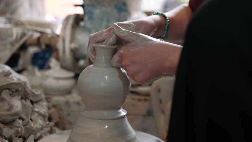 Close up of potter hands shaping a clay vase on a pottery wheel in a traditional vietnamese workshop.