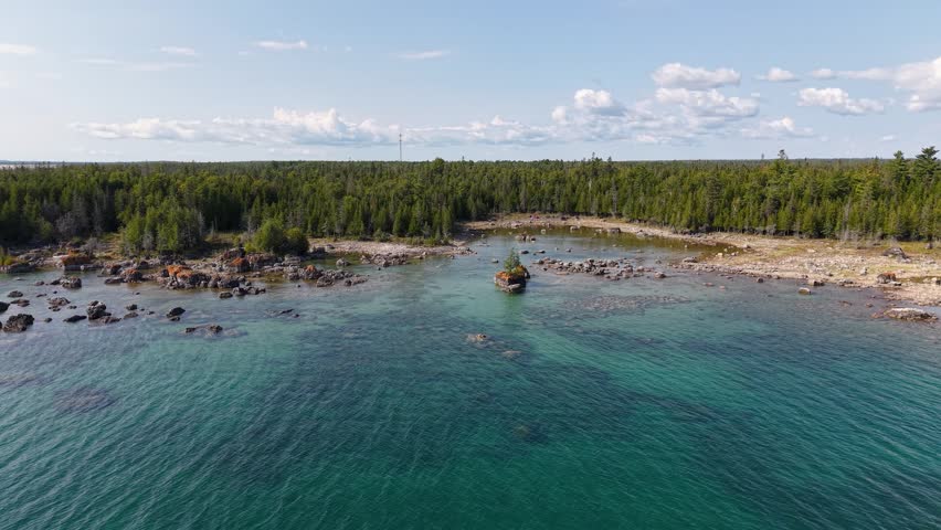Aerial view of lush woodland and rocky shoreline surrounding clear blue water, Hessel, Michigan.