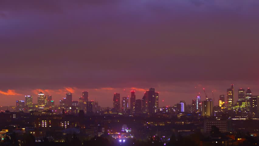 Dynamic time lapse footage of London city skyline at sunrise, revealing iconic buildings and capturing dramatic changes in sky color from purple night to brilliant yellow dawn as sun ascends through clouds.