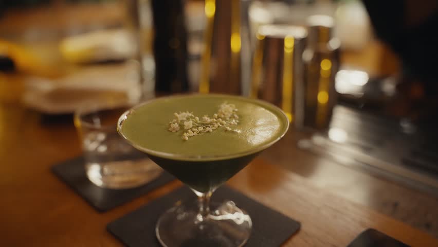 Green cocktail with flower garnish standing on bar counter