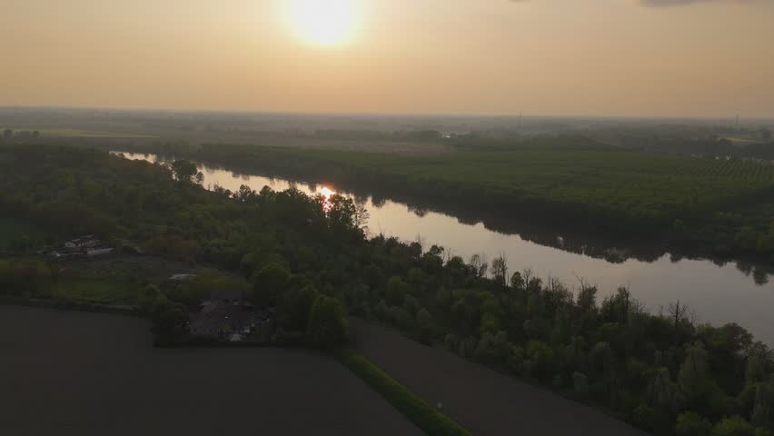 Po River crossing riparian woodland and agricultural lowlands near Isola Serafini in Piacenza province, Emilia Romagna, Italy, during sunset with reflective water and floodplain ecosystem in Po Valley