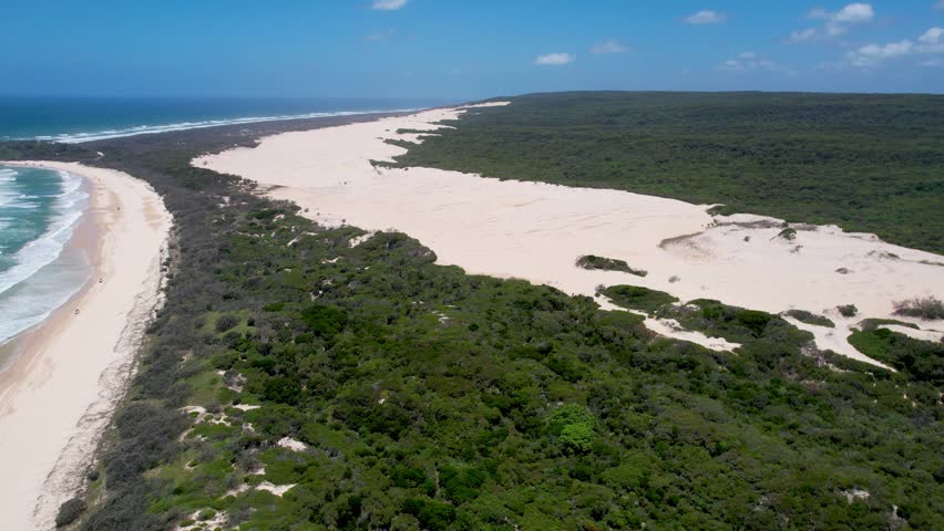 Aerial view of Tukkee Sandblow featuring vast white sand dunes surrounded by lush green forest and the turquoise ocean in K