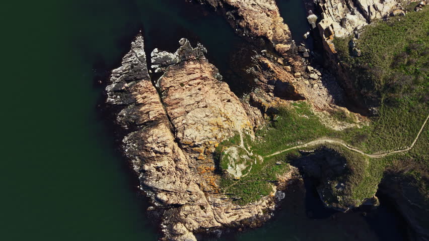 A rocky shoreline features a narrow path lined with grass leading to the water