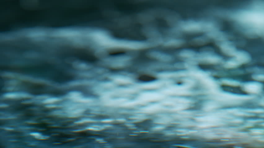 Macro close-up of a falling water drop creating a splash and ripples on a clear water surface. High-speed capture revealing fluid motion, transparency, and intricate details.