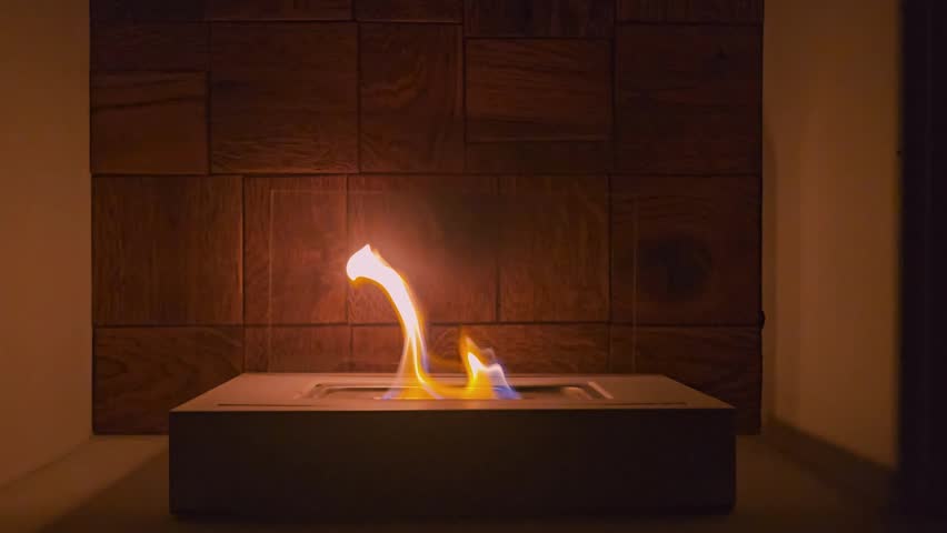 Modern tabletop bioethanol fireplace with burning flames against wooden wall closeup