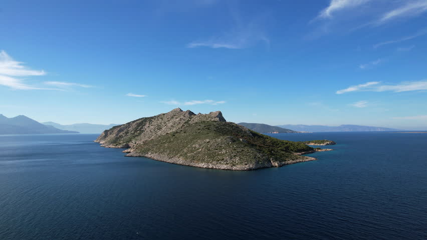 Aerial panorama of uninhabited Moni island near Aegina Greece. Steep cliffs, green pine trees, and hills under a clear blue sky.