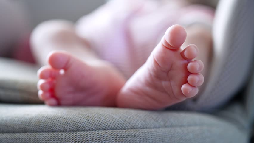Close up view of cute newborn baby feet with tiny toes resting on a soft gray cushion