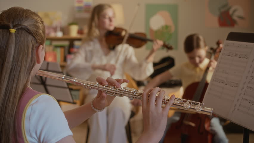 Handheld shot of children practicing flute and cello during music lesson with young female teacher playing violin. Video is ideal for promoting private music tutoring and arts education programs