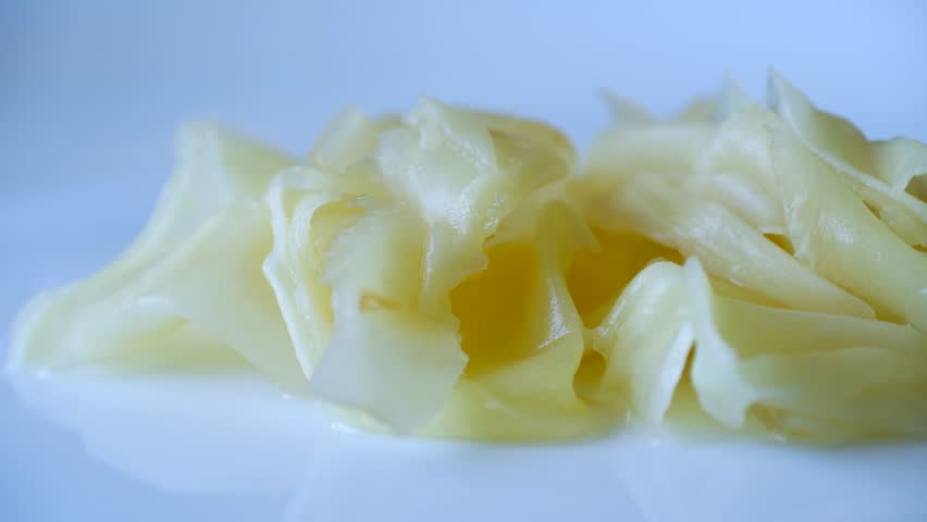 Pickled ginger gari, traditional japanese tsukemono condiment for sushi and sashimi, slowly moving on white plate, isolated on white background, revealing its texture. Pickled ginger gari on plate