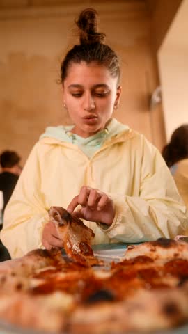Teenage woman with joyful expression eating spicy pizza confidently