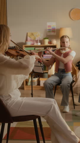 Vertical video of Caucasian female teacher playing violin and instructing two Caucasian kids playing flute and cello during home music lesson. Clip is ideal for promoting private tutoring services