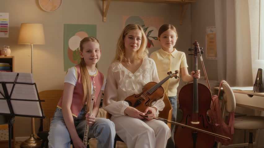 Zoom in portrait of Caucasian young female teacher and two kids holding violin, flute, and cello during music lesson at home. Video is ideal for promoting private music tutoring and arts education