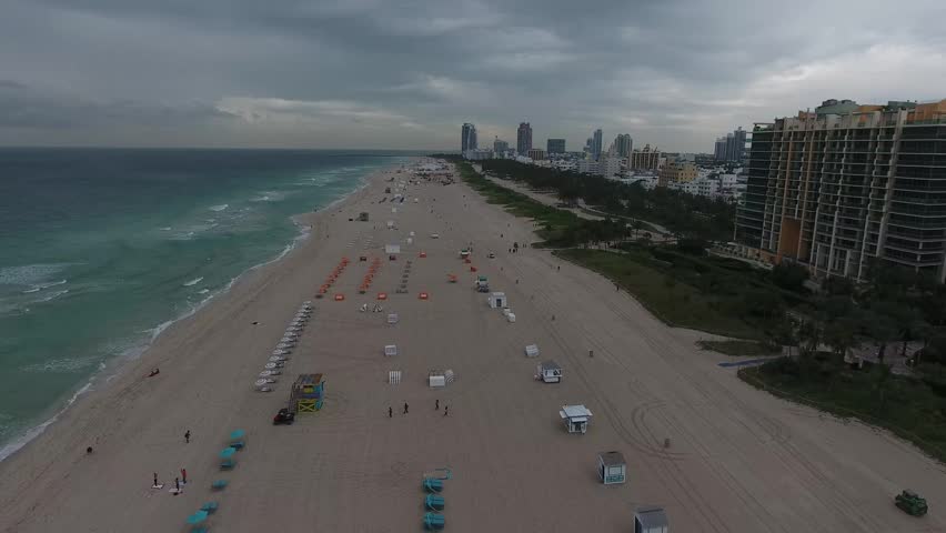 Aerial view of South Beach featuring rows of colorful umbrellas on the sand and the urban skyline under an overcast sky in Miami Beach, Florida, United States.