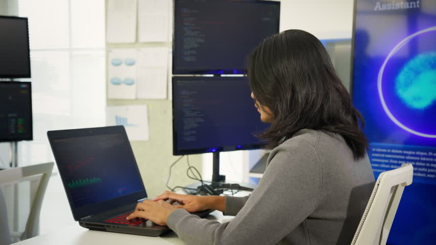Focused Asian man typing on laptop while using artificial intelligence assistant tool in modern workspace. Generative AI technology, productivity tools, individual freelance work, Tech professionals.