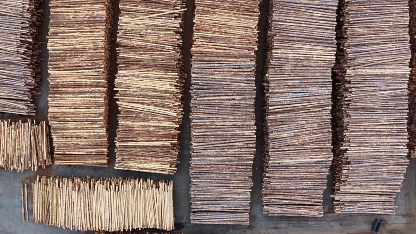 Massive timber yard with rows of stacked lumber planks and log bundles arranged in parallel patterns on industrial port surface. Washington State, USA. Aerial top down rising shot. Cloudy day.