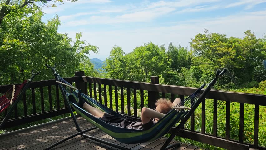 Relaxed man resting and napping in a cozy hammock in a lush green summer garden