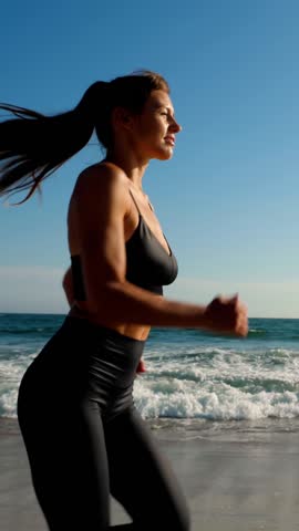 Athletic woman jogging along the beach. Vertical video.