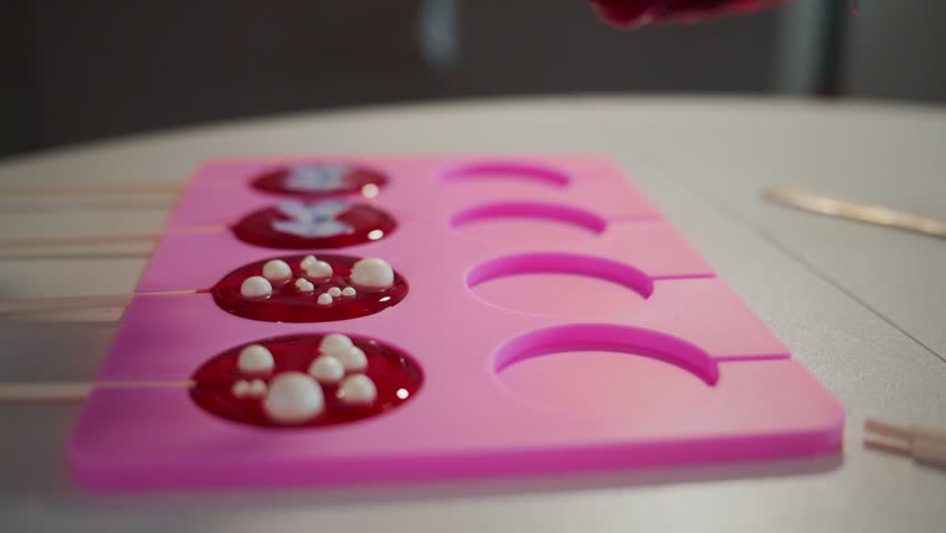 Red liquid pours into pink mold. Sweet treats form slowly. Perfect for dessert or candy ads. Close-up shot highlights texture and color. Ideal for food, cooking, or confectionery content