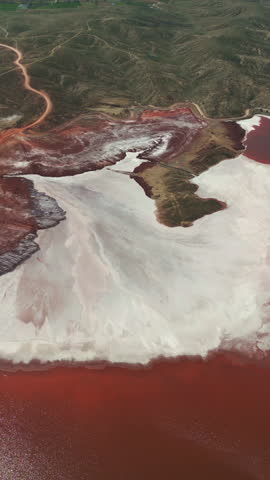 Aerial view of a red industrial pond with white mineral deposits and dark surrounding land.