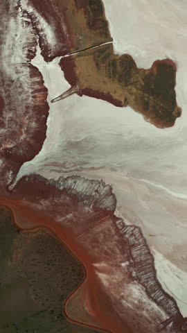 Vertical aerial footage of a red industrial pond with pale mineral deposits and dry shoreline.