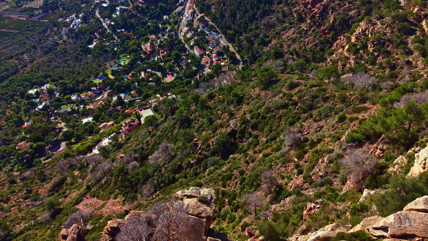 The scene shows a sloped landscape with houses nestled among trees and bushes. The sun is shining down on the area, highlighting the natural features.