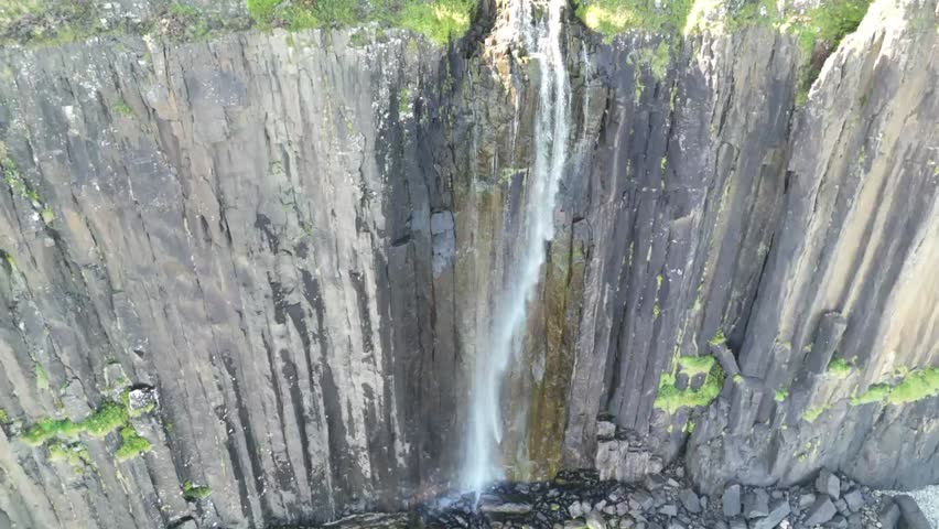 Waterfall flowing off dramatic cliffs into the sea in Scotland, surrounded by rugged coastal beauty 