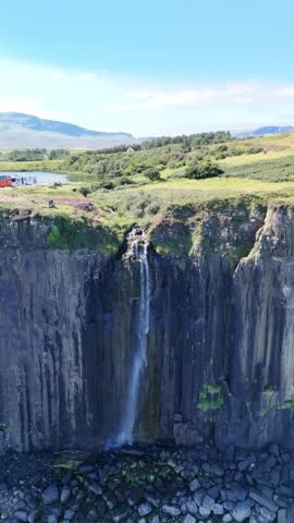 Waterfall flowing off dramatic cliffs into the sea in Scotland, surrounded by rugged coastal beauty 