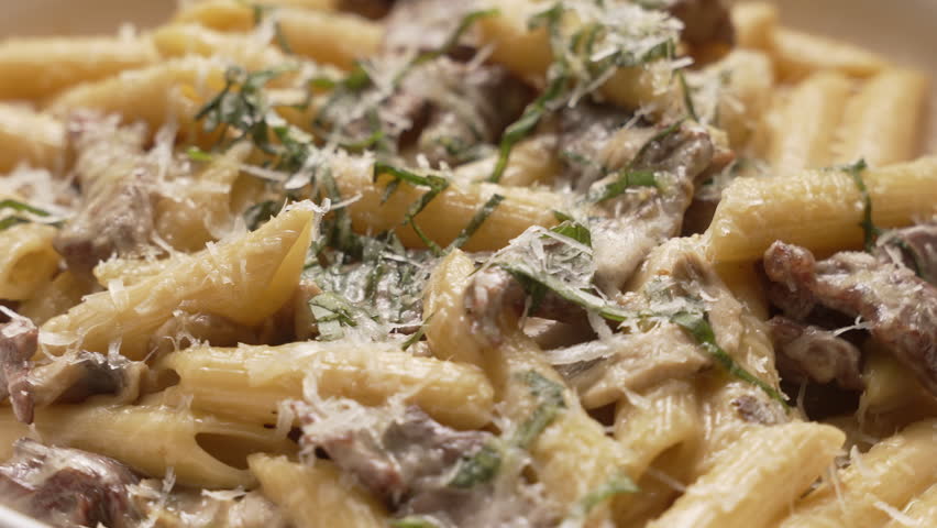 Freshly made penne pasta with chicken, mushrooms, and pesto in a white bowl rotating slowly, fa01