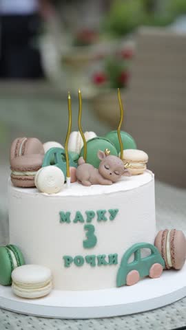 A custom decorated white birthday cake with green macarons and candles for a three year anniversary celebration, birthday cake decoration, third birthday party, custom sweet dessert.
