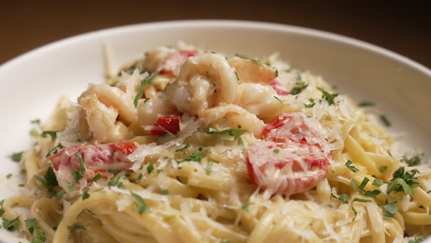 Creamy shrimp pasta with tomatoes and herbs served on a white plate in a restaurant, fa01