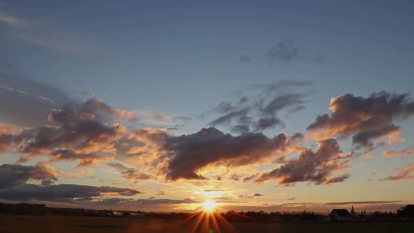 Brilliant sunstar sunset over flat rural landscape with dramatic orange-lit clouds, timelapse