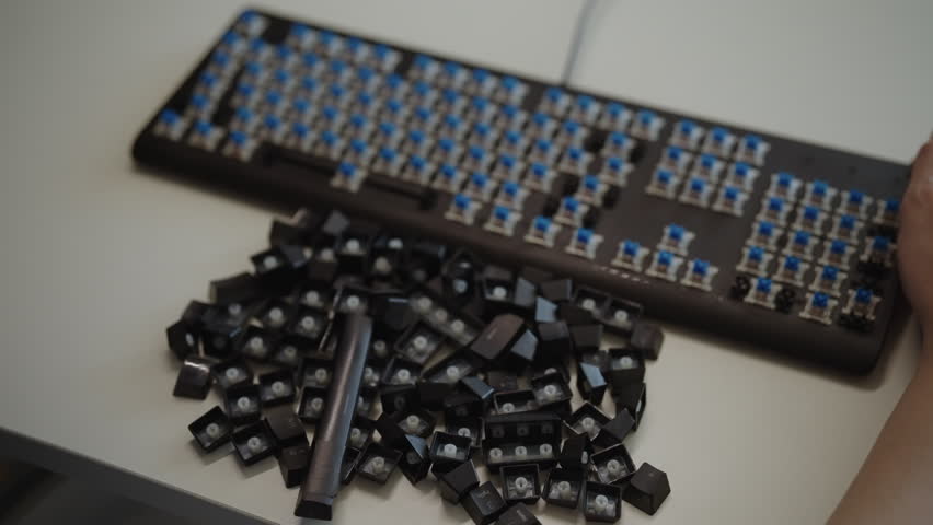 Technician removing keycaps from mechanical keyboard with special tool for cleaning and maintenance, dropping keys into container. Geek culture and electronic device repair concept