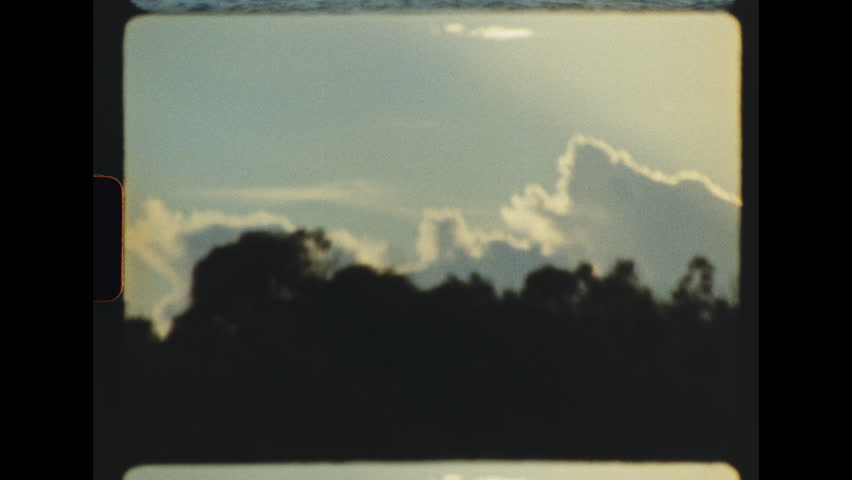 Slow camera pan moving across glowing golden sunset clouds above a dark silhouette of trees on the horizon captured on retro super 8 film