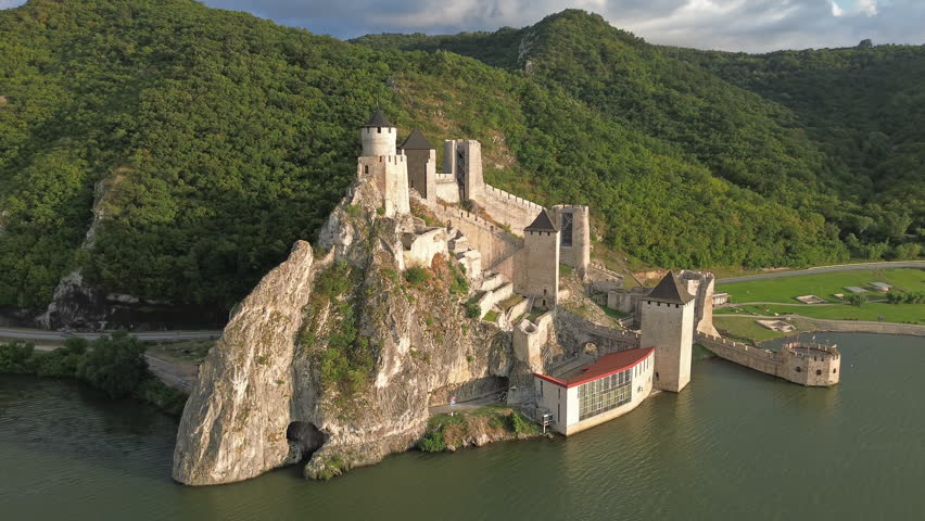 Aerial around view of Golubac medieval fortress on cliff above Danube river at sunset, historic landmark in Serbia, 4k
