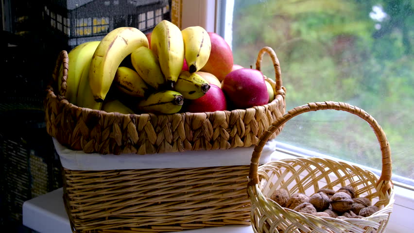 Wicker baskets with bananas apples and walnuts on bright windowsill in cozy home kitchen