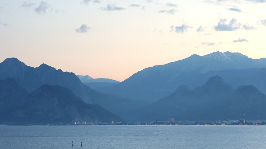 Timelapse of dusk light over a calm lake with layered mountains in silhouette.