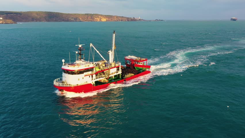 Red fishing boat with nets and catch load on deck navigating northern entrance of Bosphorus Strait returning from Black Sea at sunset