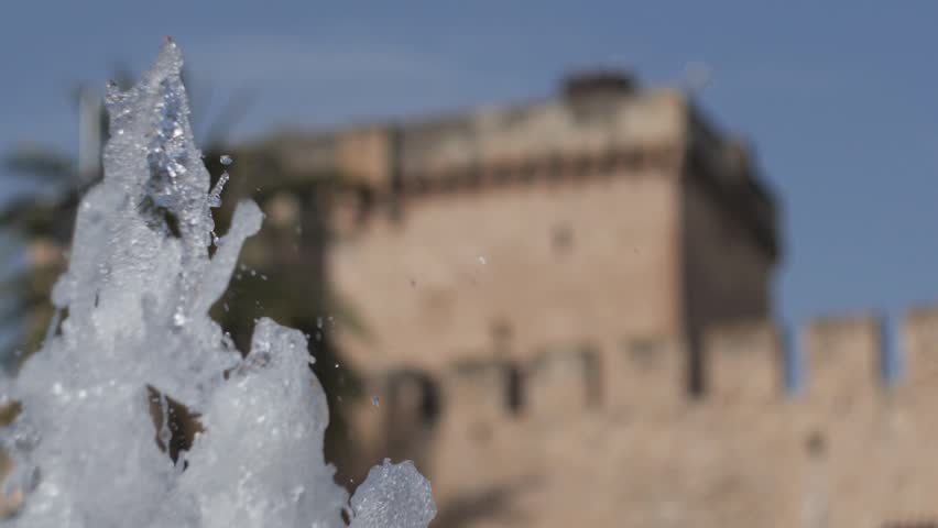 Super slow motion of the jets of a fountain with the Altamira Palace tower out of focus in the background. Elche, Spain.