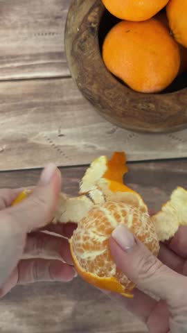 Hands peel fresh orange from bowl on rustic wooden table, revealing juicy fruit transformation