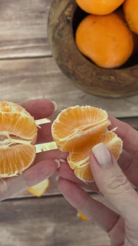 Peeling and separating juicy oranges on wooden table – hands show fresh citrus in action