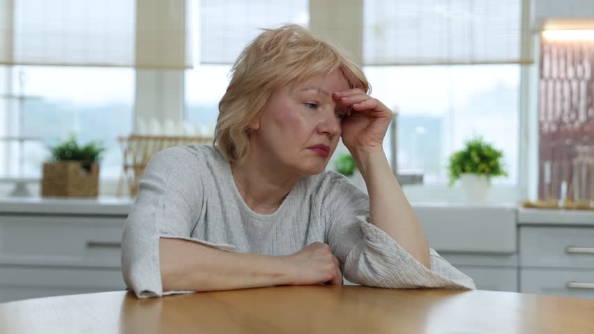 Tired senior woman at table in kitchen
