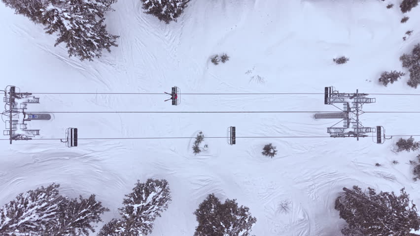 The ski lift is surrounded by a blanket of snow, with trees on both sides. The scene shows the lift going over the snowy ground, indicating a cold winter day in the mountains.