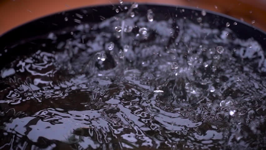 Rain drops landing in a black bucket of water in slow motion close up