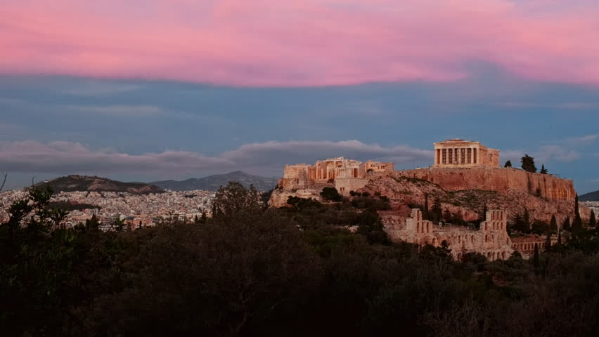 The Acropolis of Athens and the Parthenon prominently illuminated at dusk under a pink and blue sky in Athens, Greece
