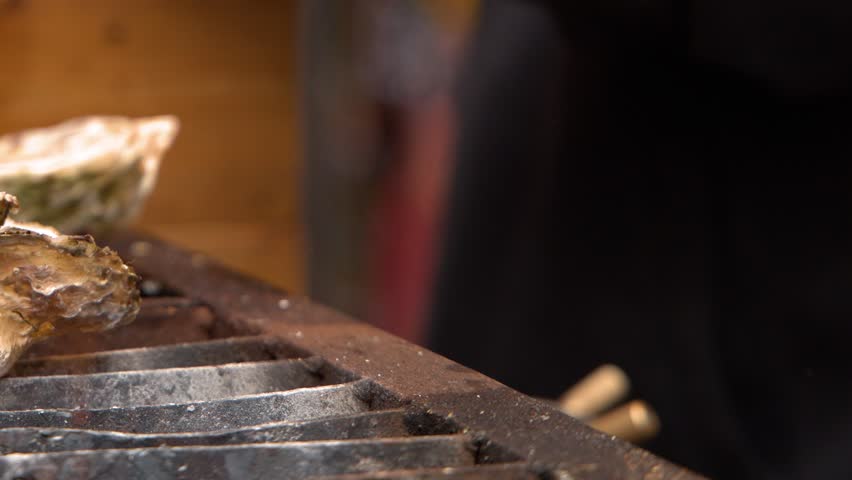 Close-up shot of large oysters cooking on a metal grill with flickering orange flames.