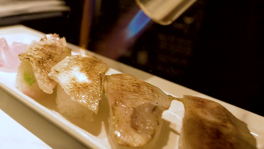Close-up shot of a chef searing fresh nigiri sushi with a blue blowtorch flame