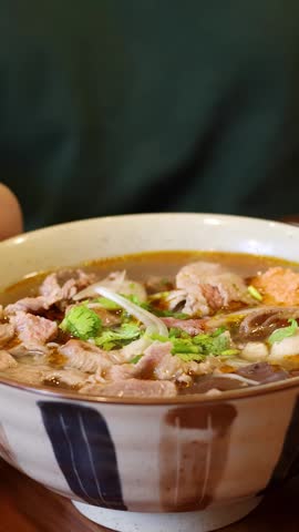Static close-up shot of steaming Vietnamese beef noodle soup served in a ceramic bowl.