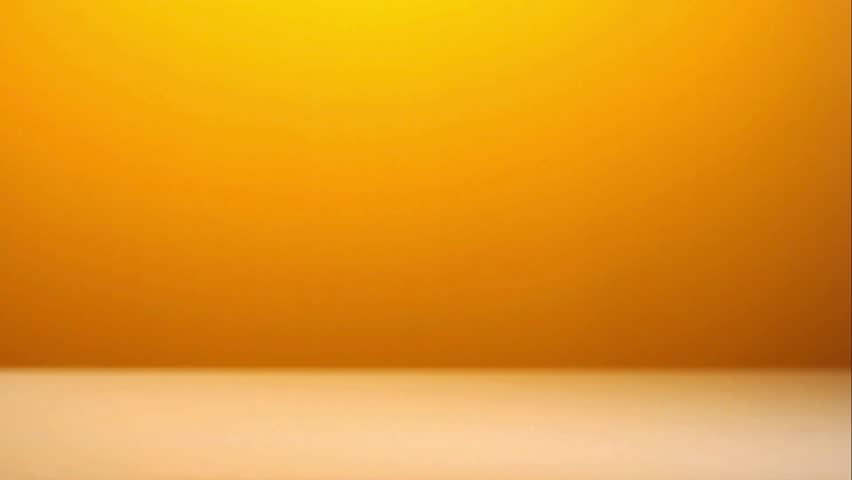 Multiple brass rifle and pistol bullets falling and bouncing on a white surface with a vibrant yellow and orange gradient background in slow motion