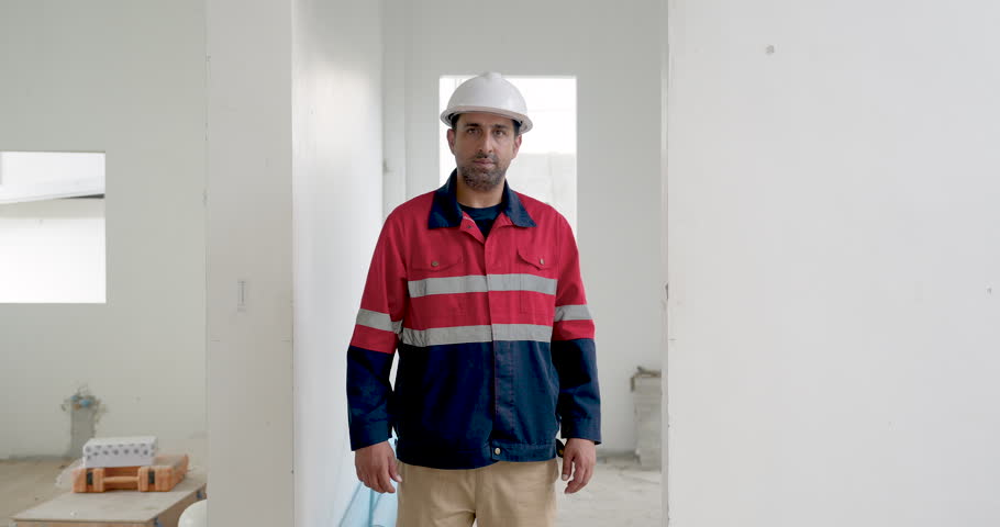 Asian male construction worker stands inside unfinished building with crossed arms, presenting confident site supervision portrait, workplace safety, quality control, project progress readiness